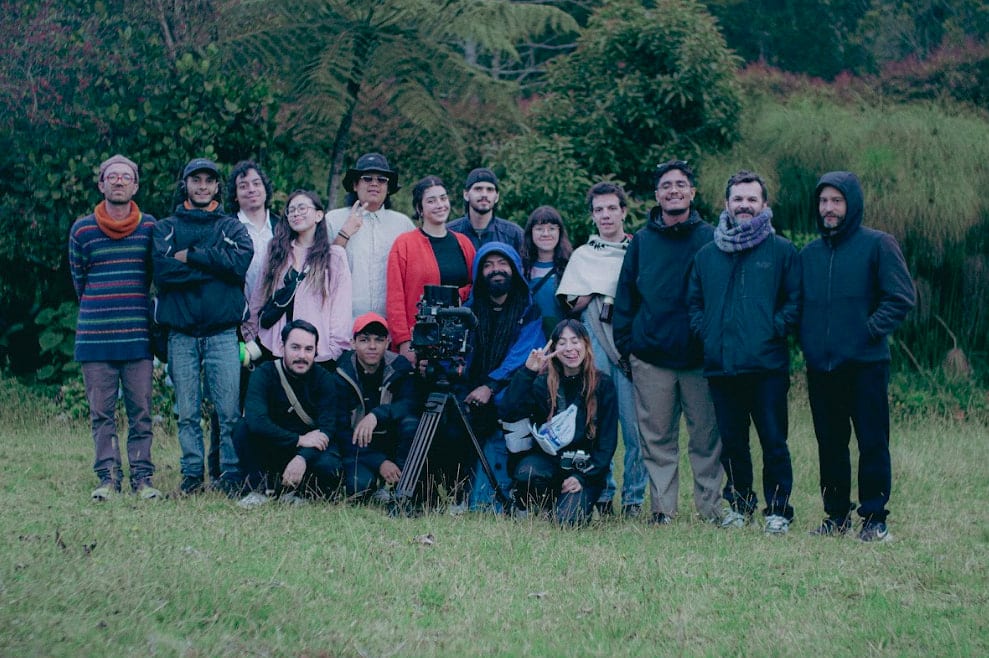 Integrantes de Coocine de pie junto a una cámara de cine sobre trípode, en el pasto frente al bosque